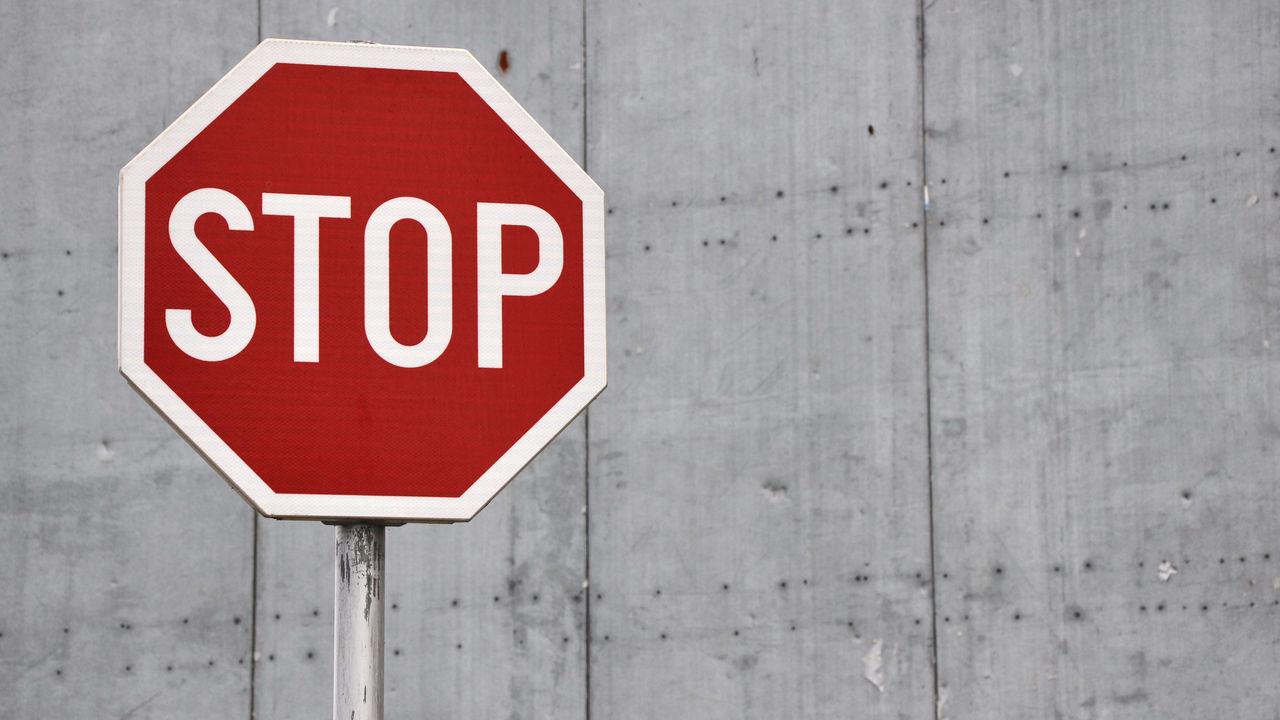 A red and white stop sign on a concrete wall.