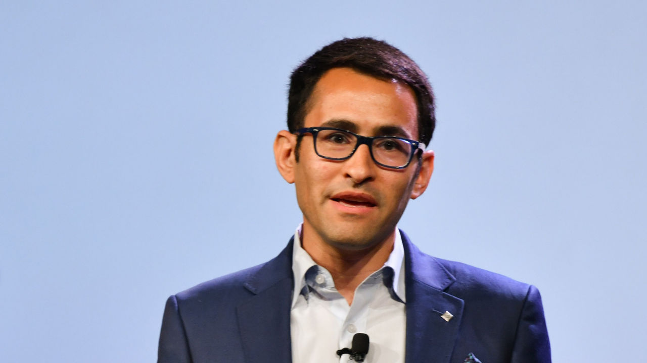 A man in a suit and glasses is speaking on stage.