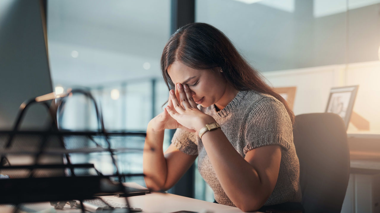 A woman is sitting at a desk with her hand on her face.