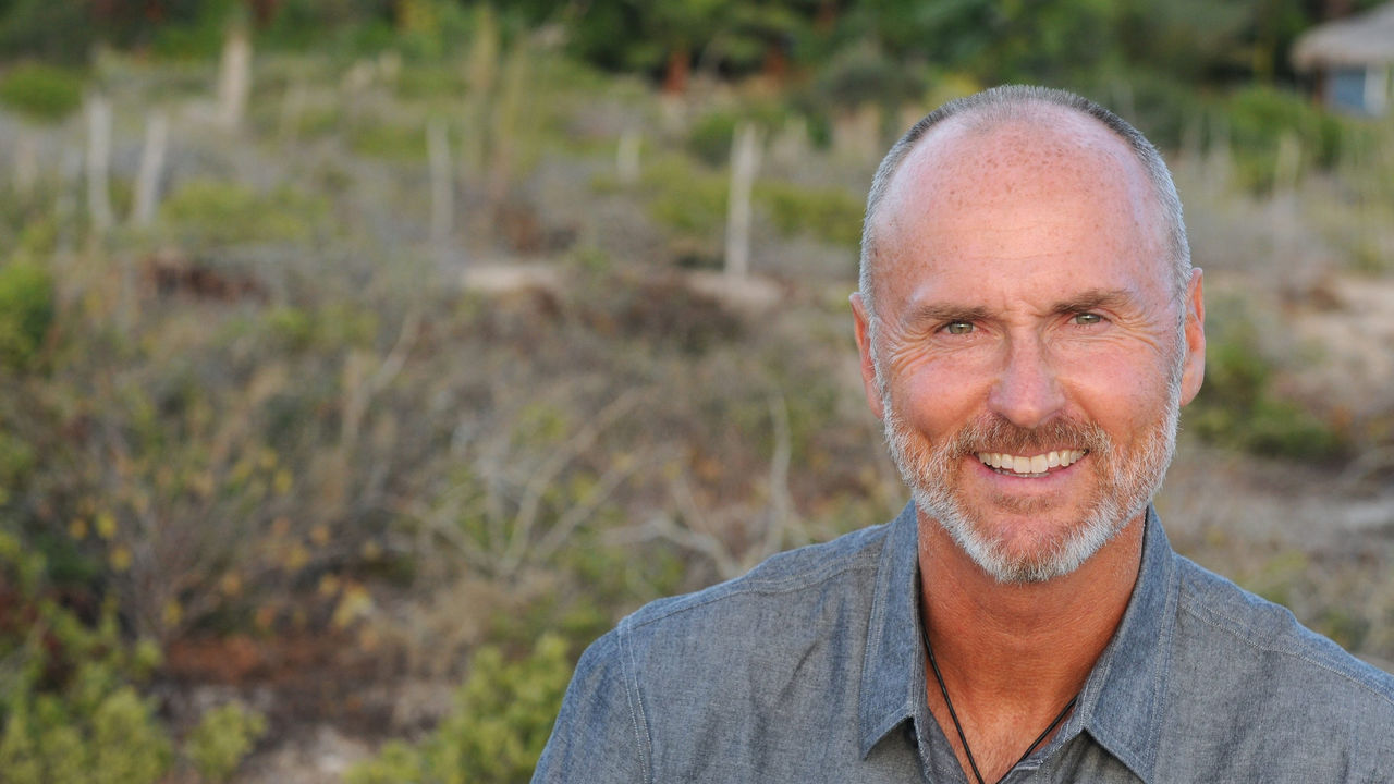 A man in a gray shirt smiling in a field.