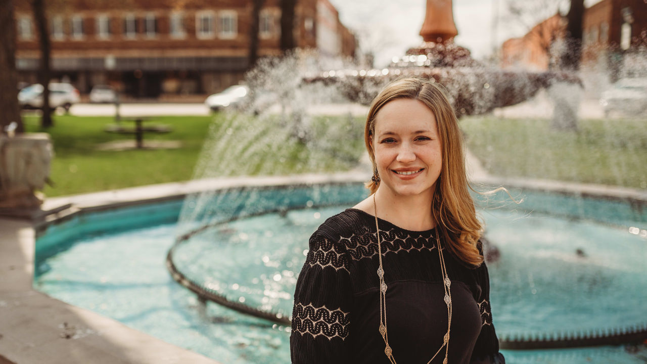 A woman smiles in front of a fountain.