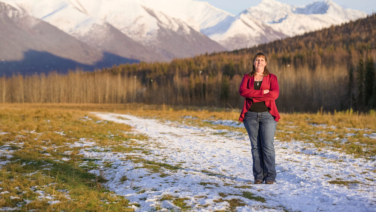 A woman standing in a snowy field with mountains in the background.