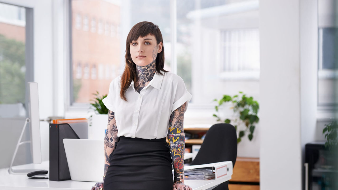 A woman with tattoos standing in front of a desk in an office.