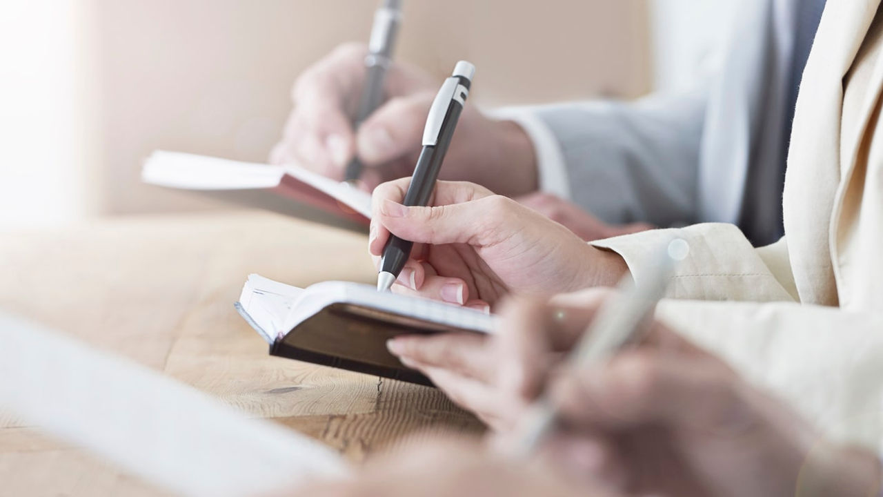 A group of business people writing in a notebook.