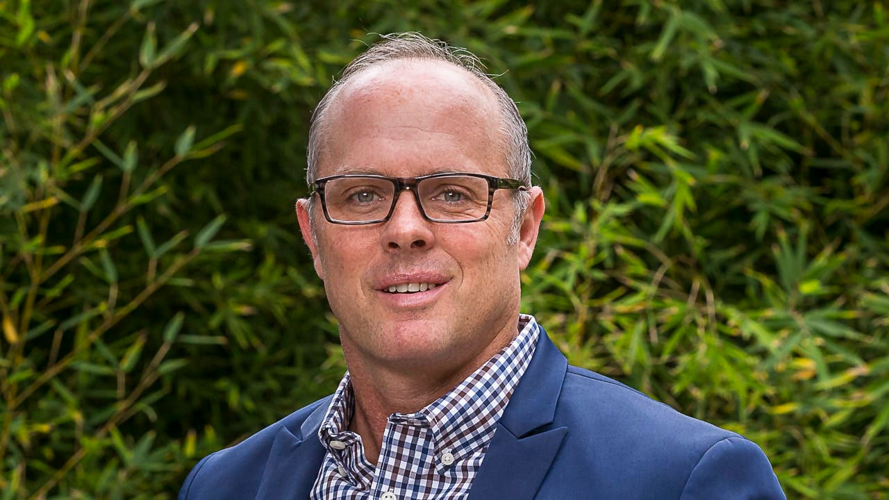 A man in a blue suit standing in front of bushes.