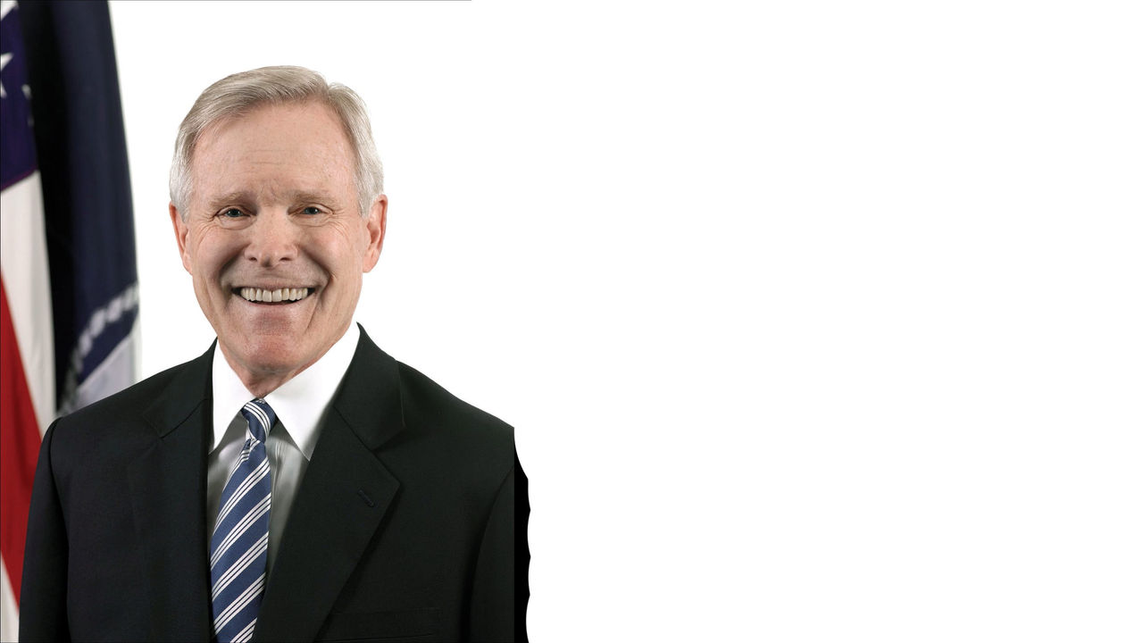 A man in a suit and tie is smiling in front of an american flag.