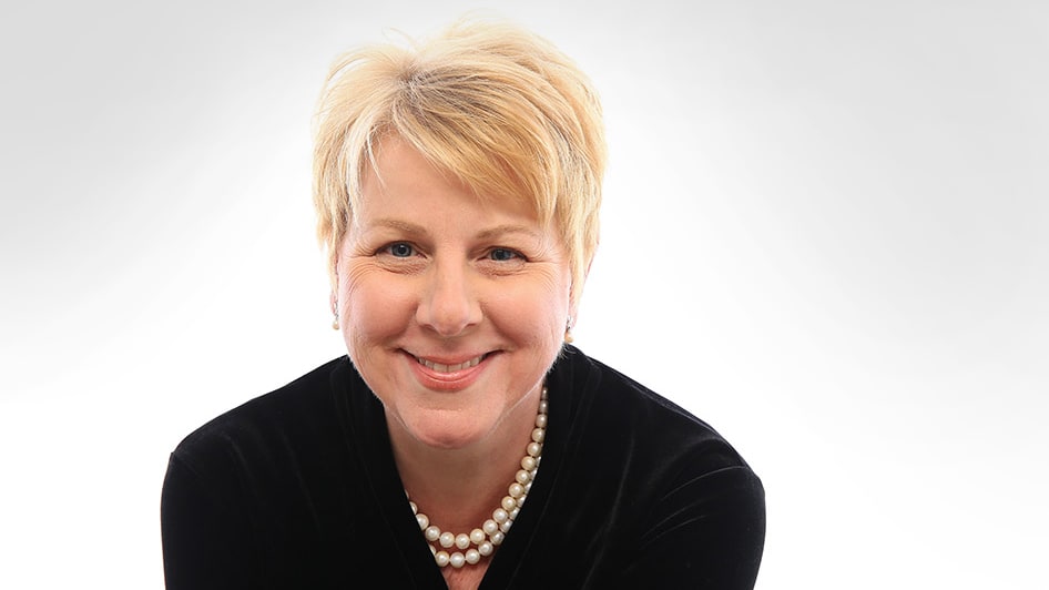 A smiling woman wearing a black jacket and pearls.