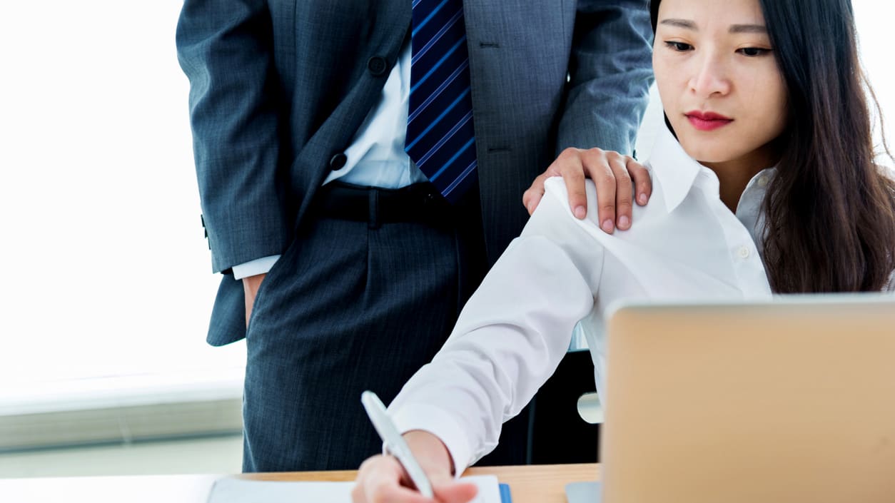 A woman in a business suit and a man in a suit looking at a laptop.