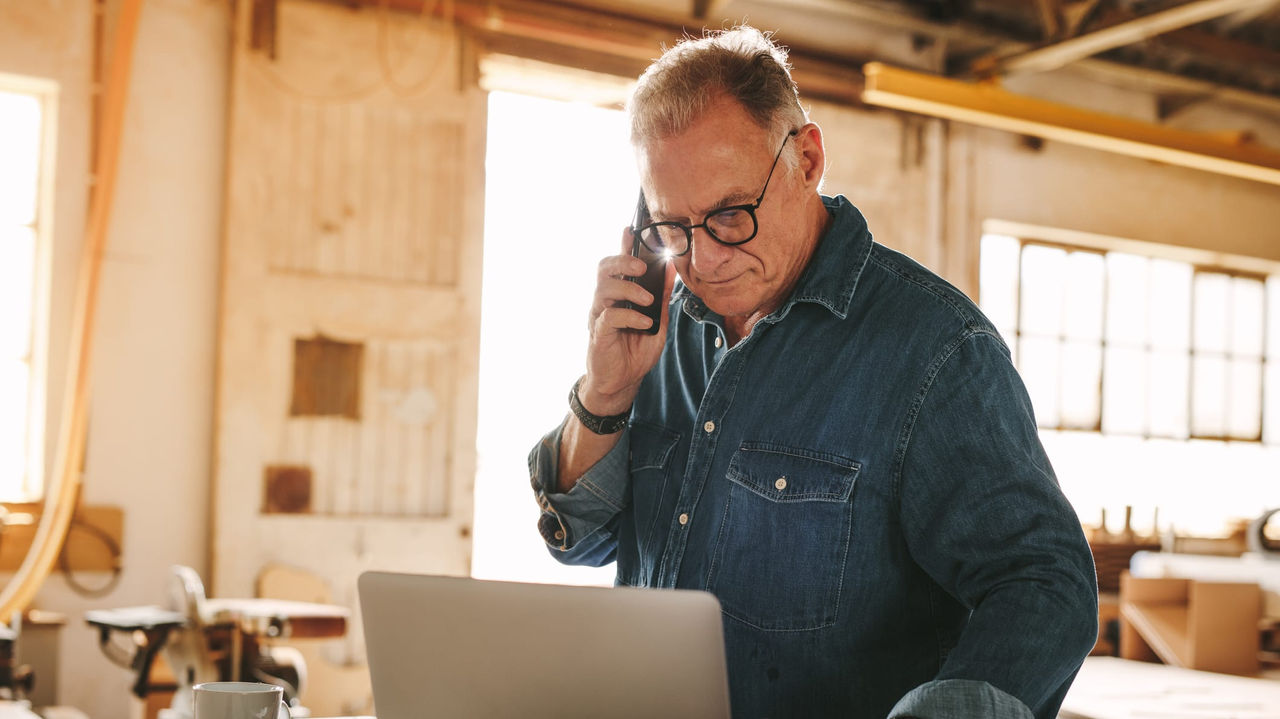 An older man on a cell phone in a workshop.