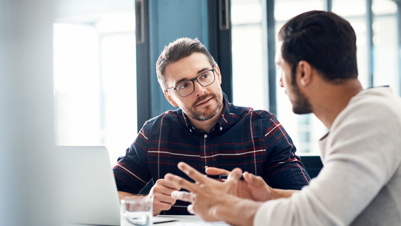 Two men talking at a table in an office.