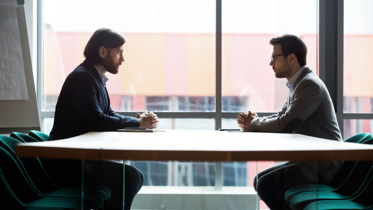 Two businessmen talking at a table in an office.
