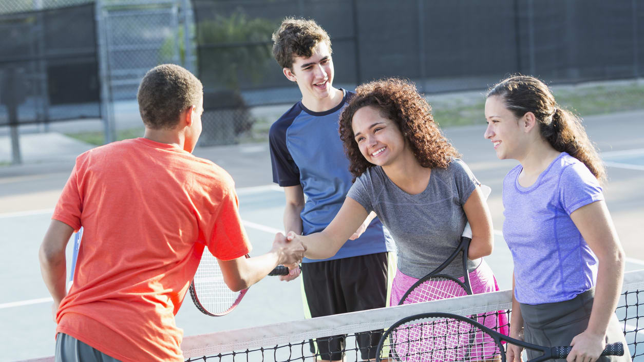 A group of young people shaking hands on a tennis court.
