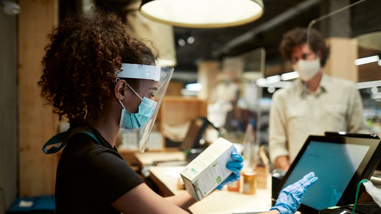 A woman wearing a mask and gloves at a checkout counter.