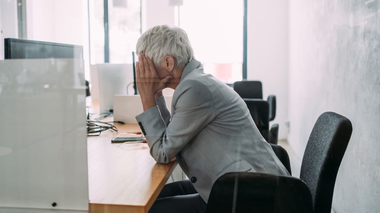 A woman covering her face while sitting at a desk.