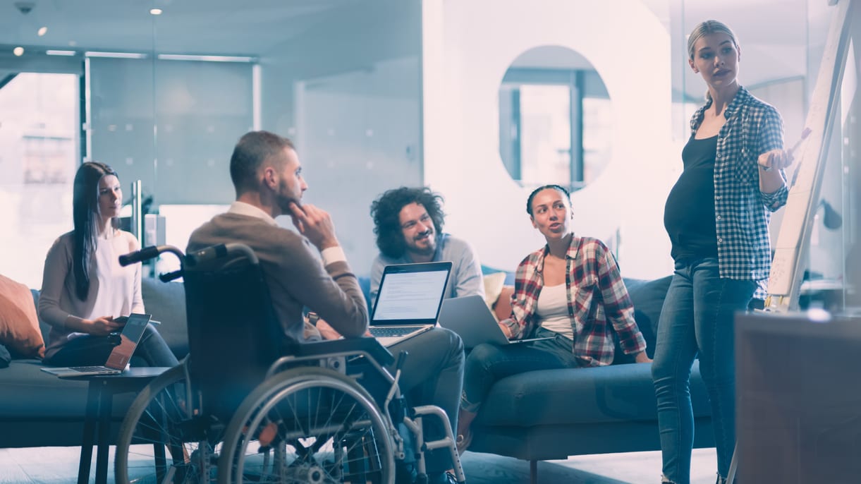 A group of people sitting around a table with a woman in a wheelchair.