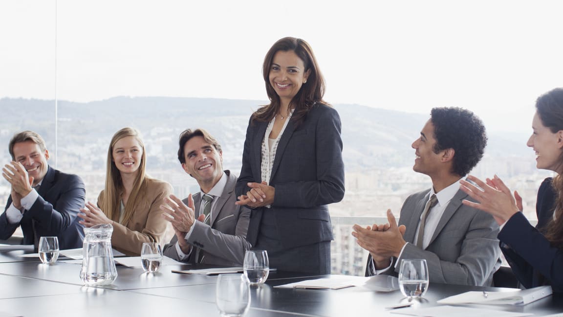 A group of business people clapping at a conference table.