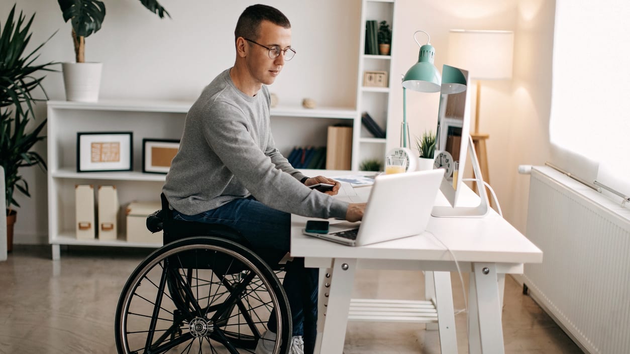 A man in a wheelchair using a laptop at home.