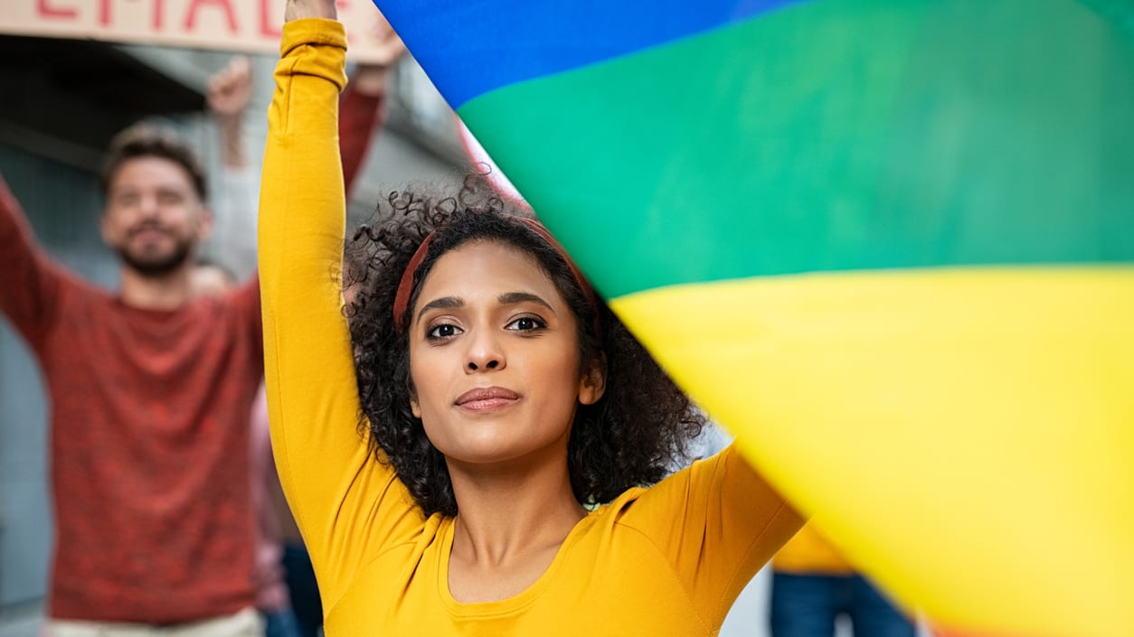 A woman holding up a rainbow flag in front of a crowd of people.