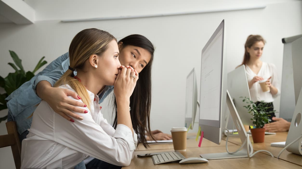 Two women hugging each other while sitting at a desk in an office.