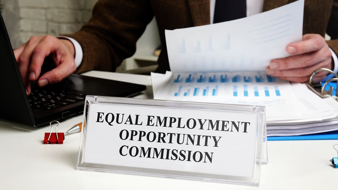 A man sitting at a desk with a sign that says equal employment opportunity commission.