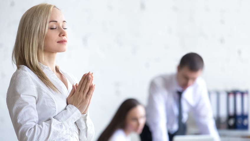 A woman is praying in front of a group of people in an office.