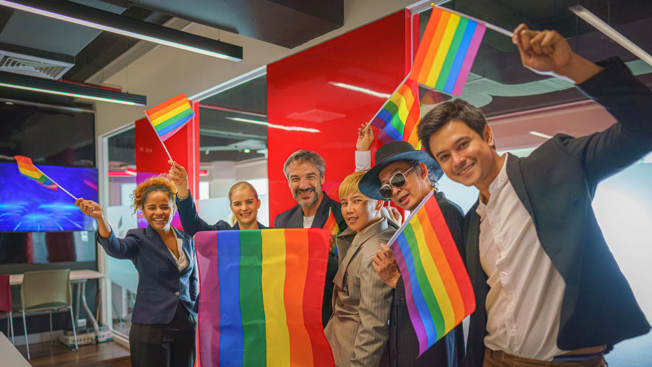 A group of people waving rainbow flags in an office.