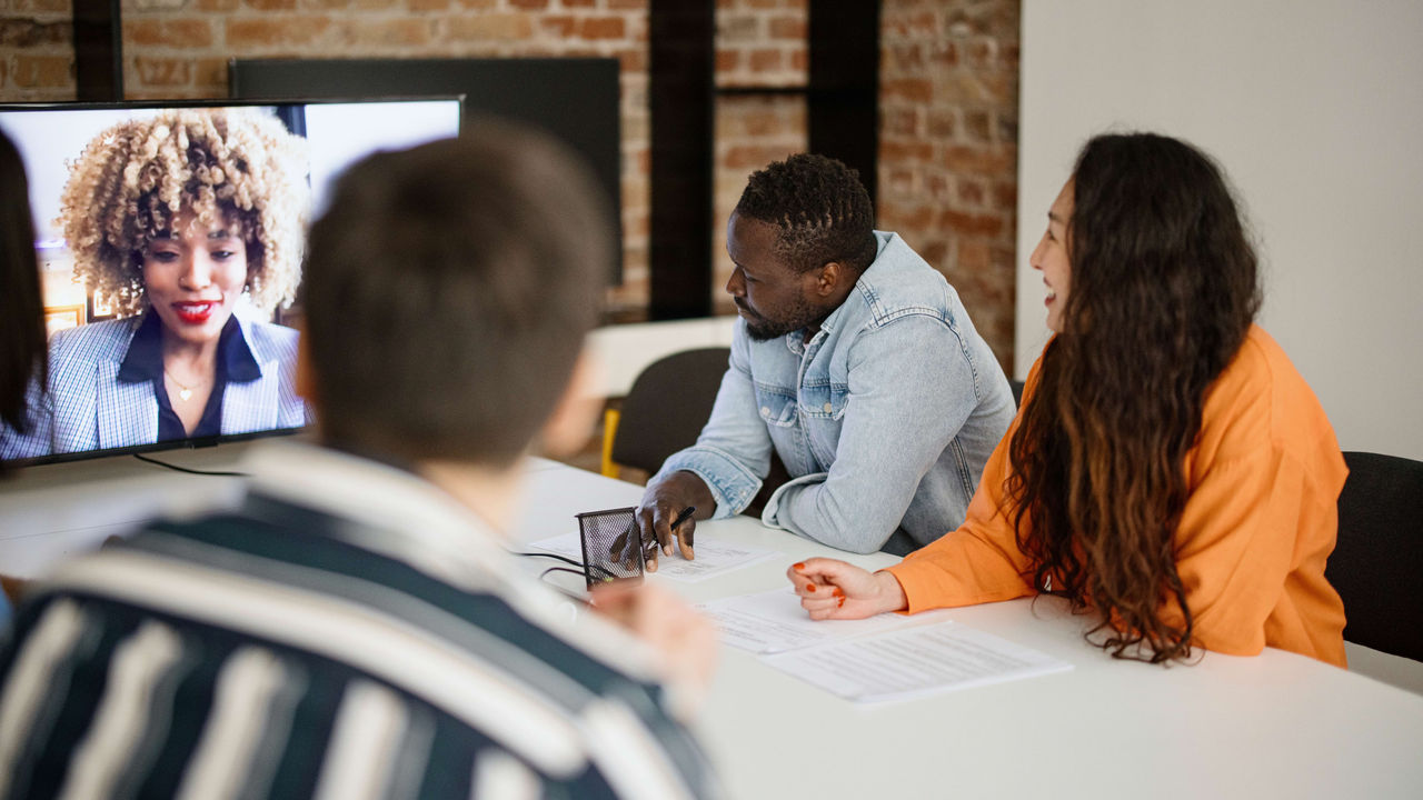 A group of people sitting around a table watching a video conference.