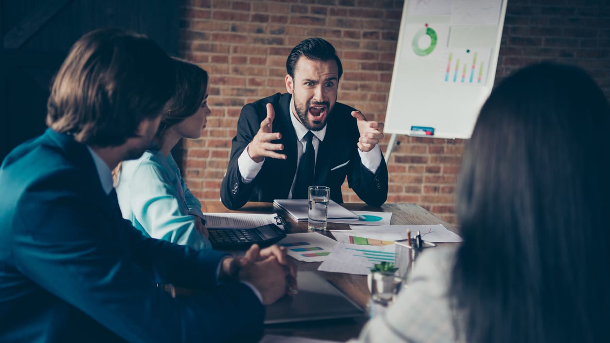 A group of business people sitting around a table and yelling at each other.