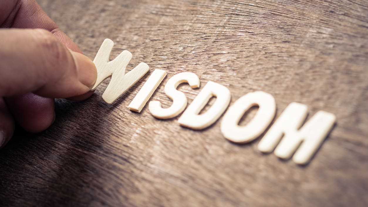 A person holding the word wisdom on a wooden table.