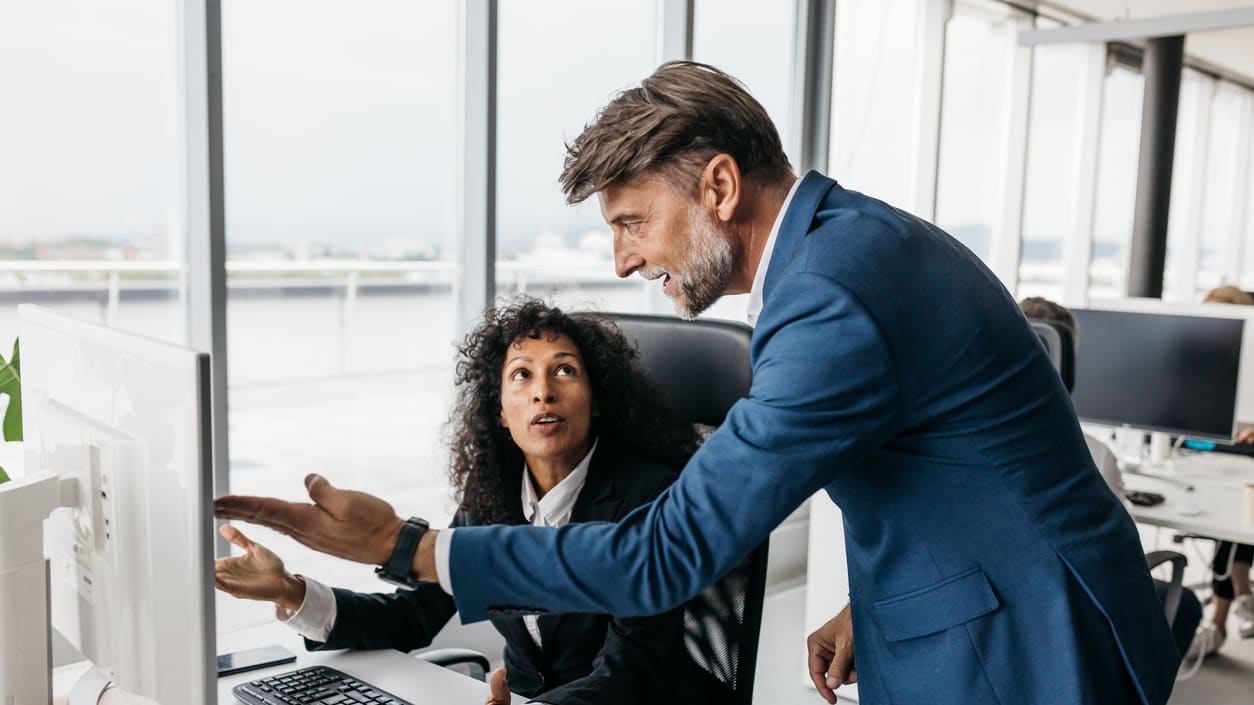 Two business people pointing at a computer screen in an office.