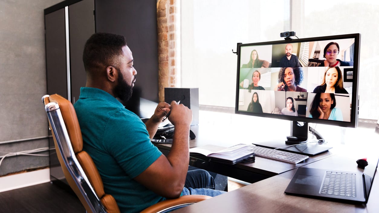 A man sitting at a desk with a video conference on his computer.