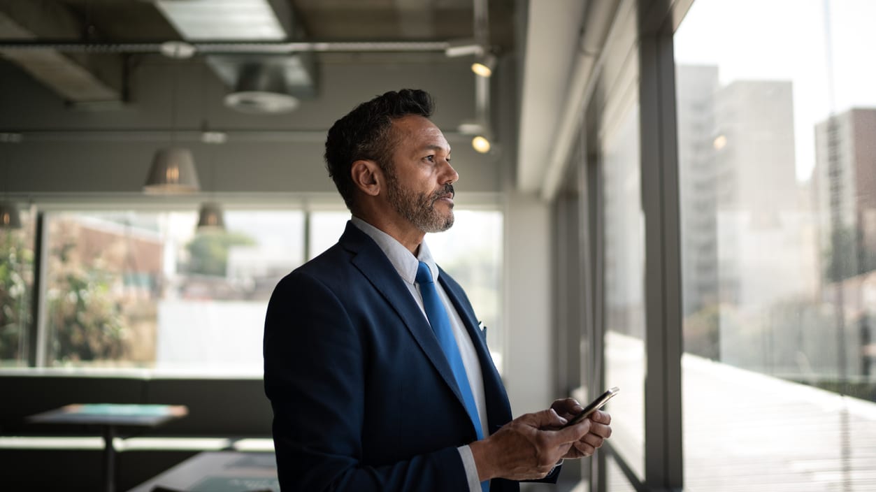 A businessman in a suit standing by a window looking at his phone.