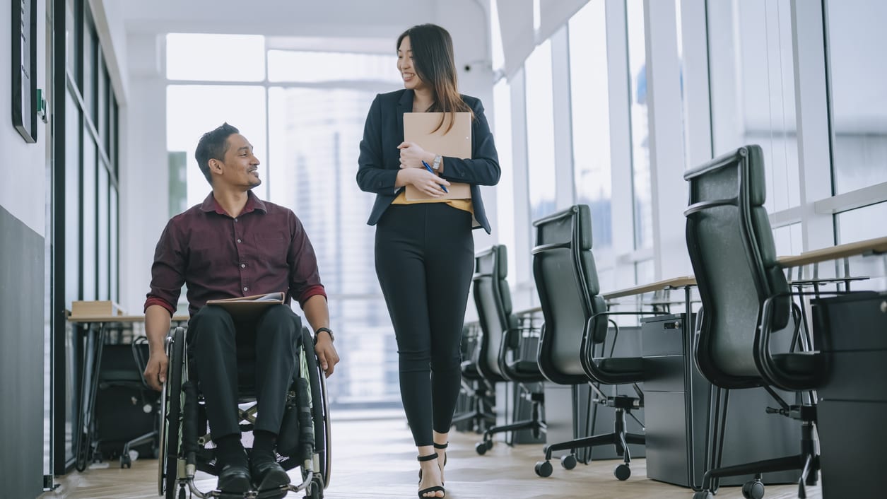 A man in a wheelchair is talking with a woman in an office.