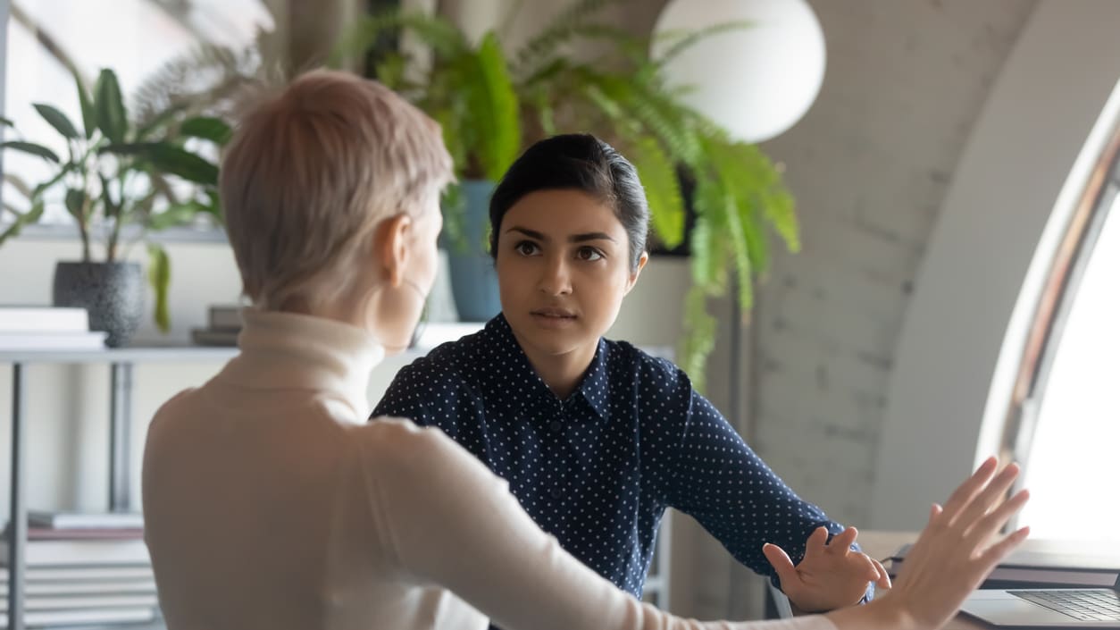 Two women talking at a table in an office.