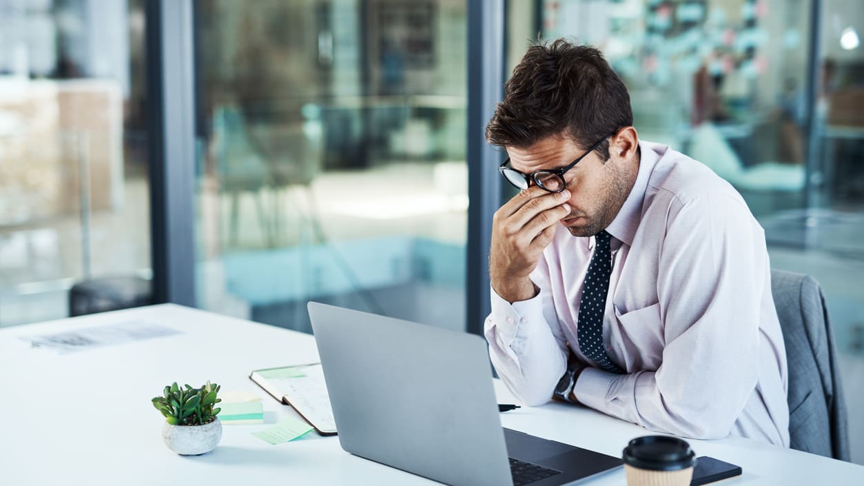 A businessman sitting at a desk with his hands on his face.