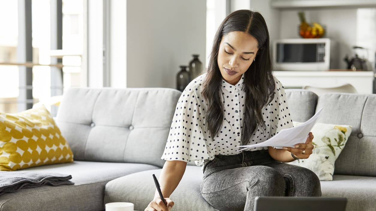 A woman sitting on a couch with a laptop and papers.