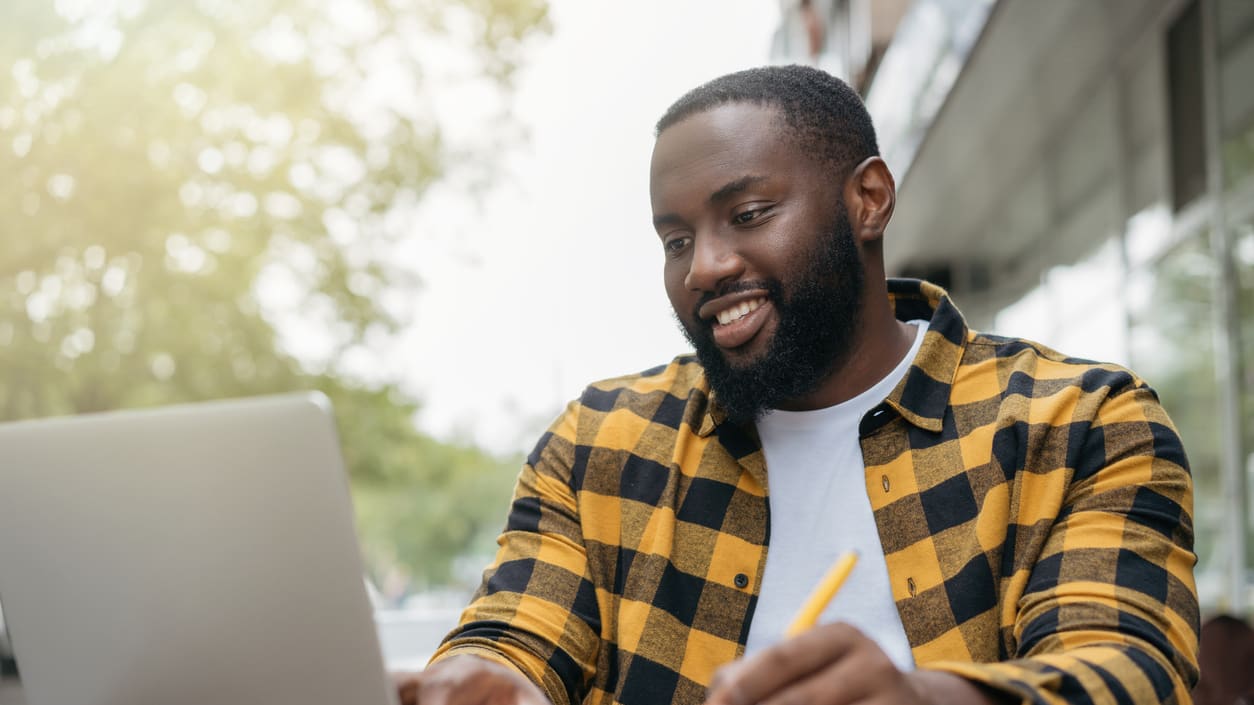 A man sitting at a table with a laptop and a pen.