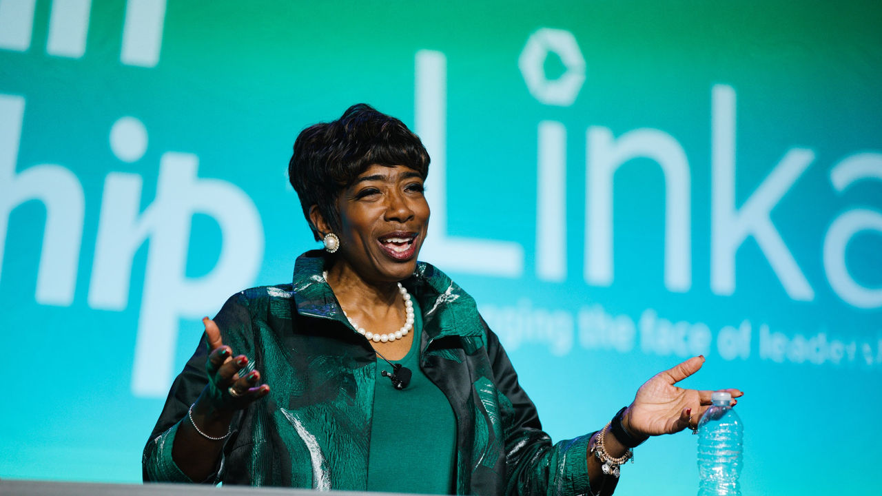 A woman in a green jacket is speaking at a conference.