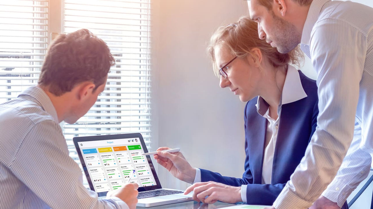 Three business people looking at a spreadsheet on a laptop.