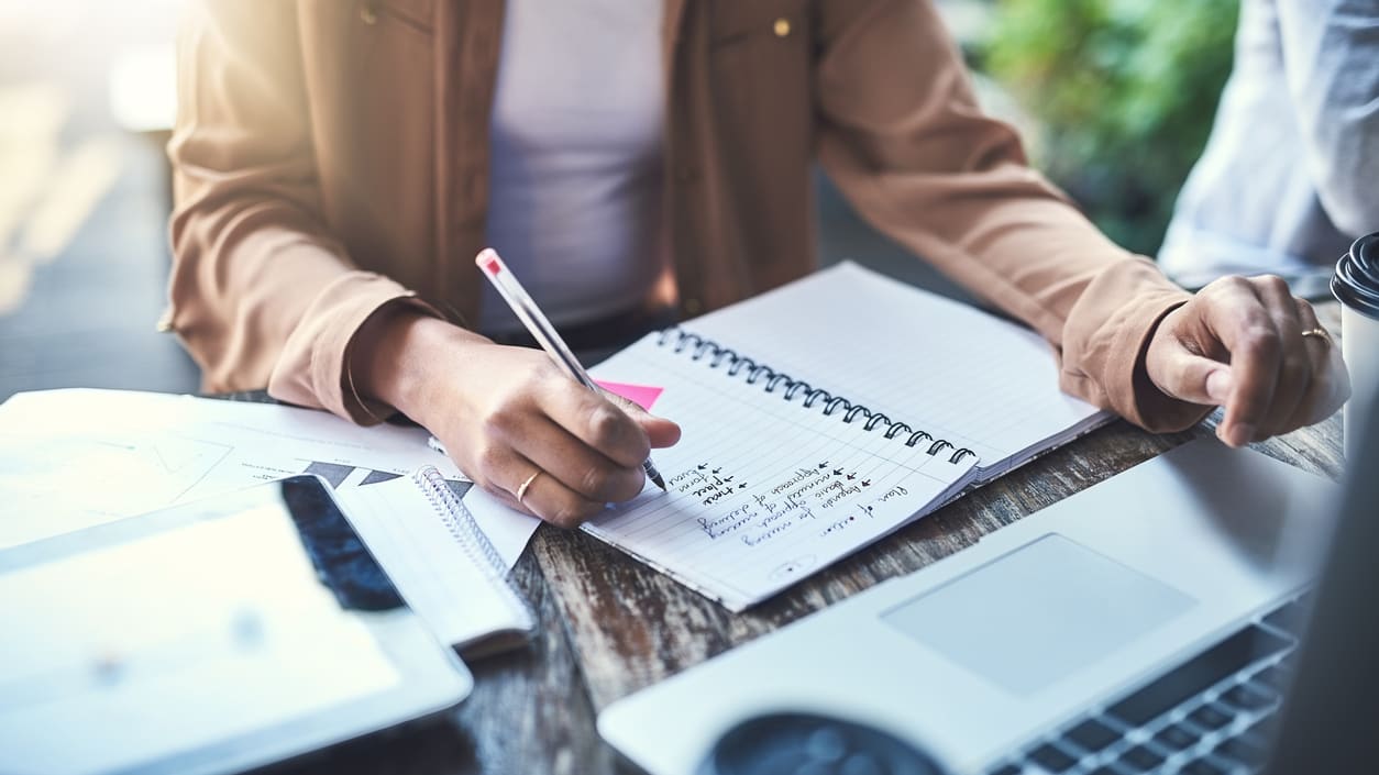 A woman is writing on a notebook while sitting at a desk.