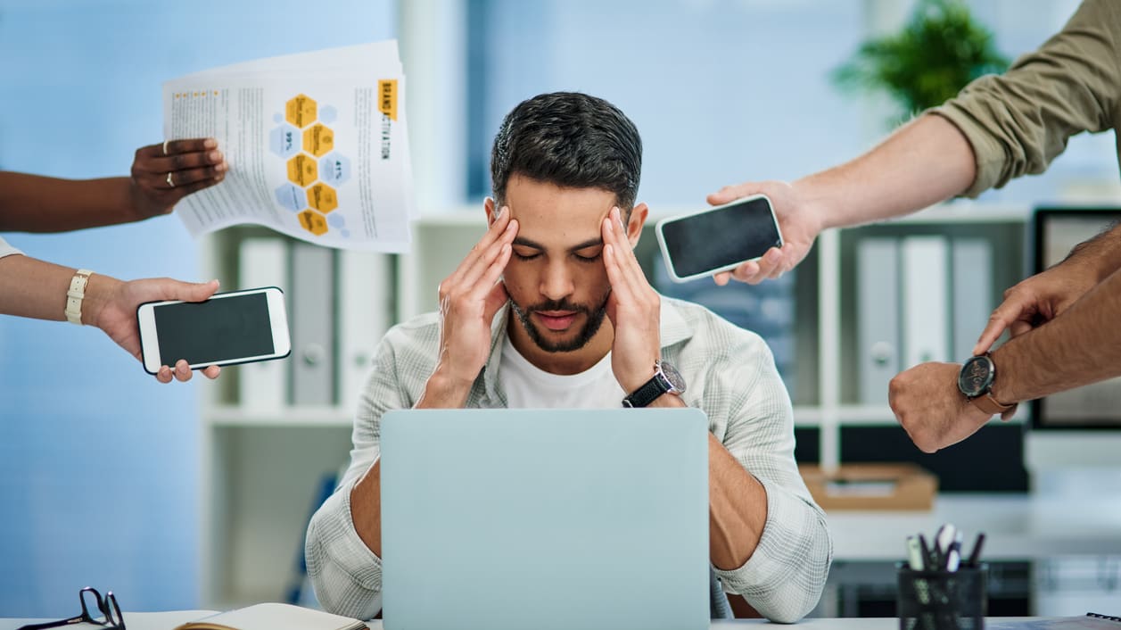 A man with his head covered by a group of people in front of a laptop.