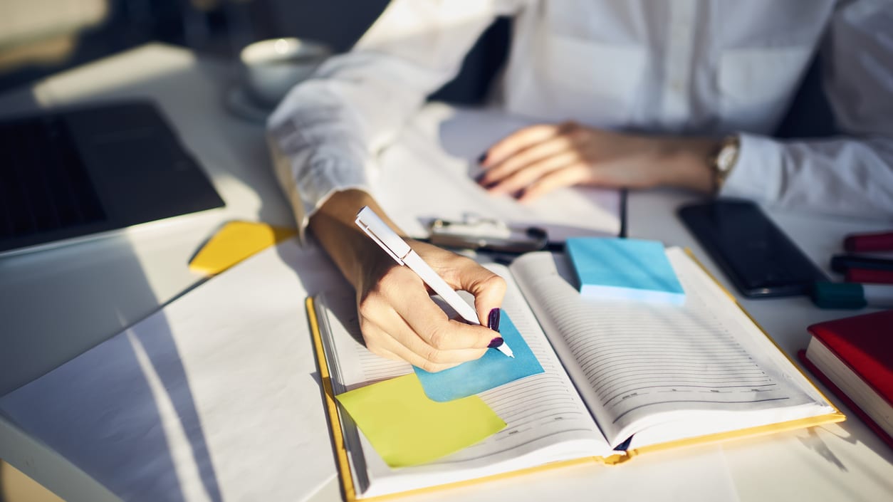 A woman is writing on a notebook at a desk.