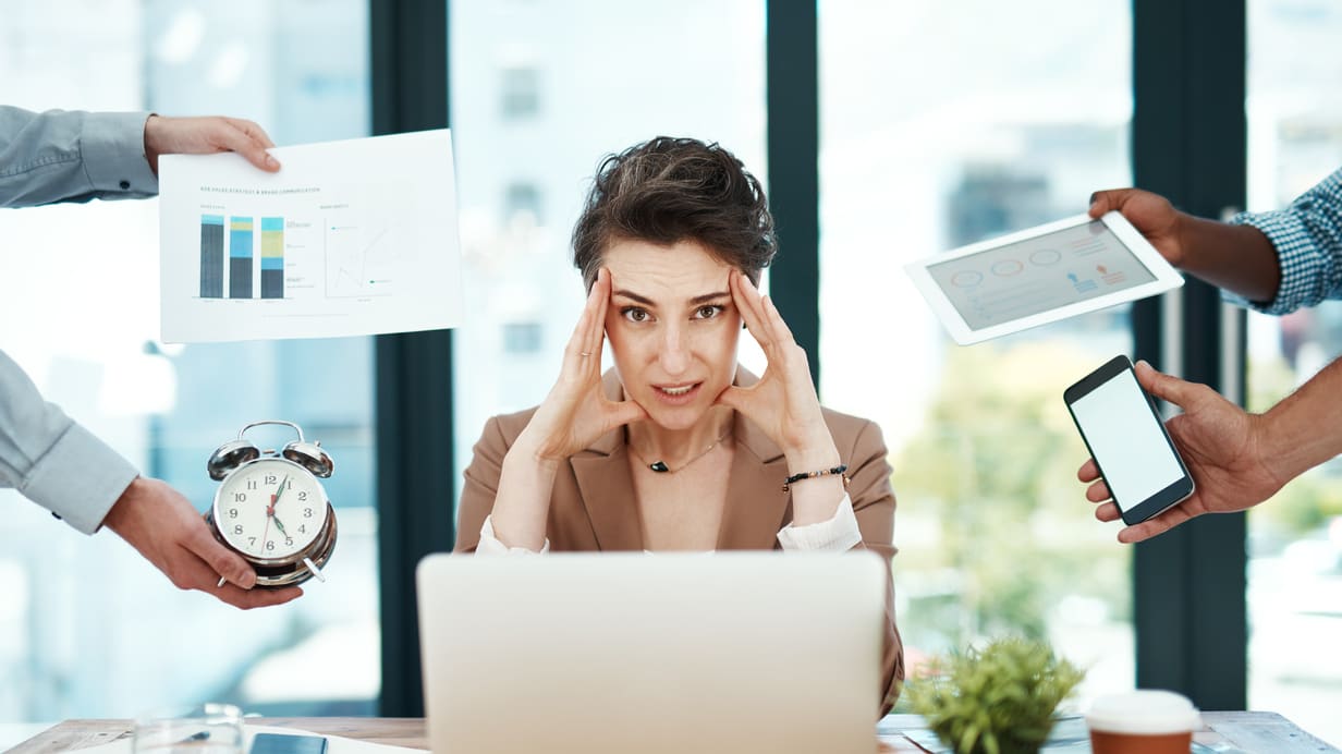 A woman sitting at a desk with a laptop, phone, and other things around her.