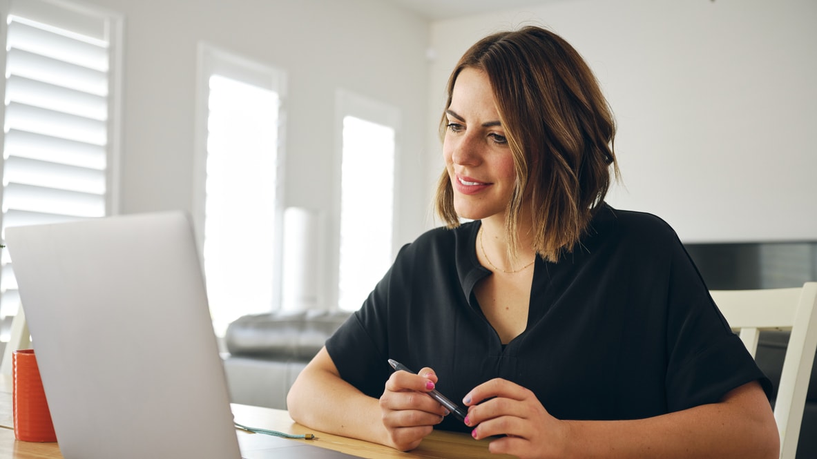 A woman sitting at a table with a laptop and a pen.