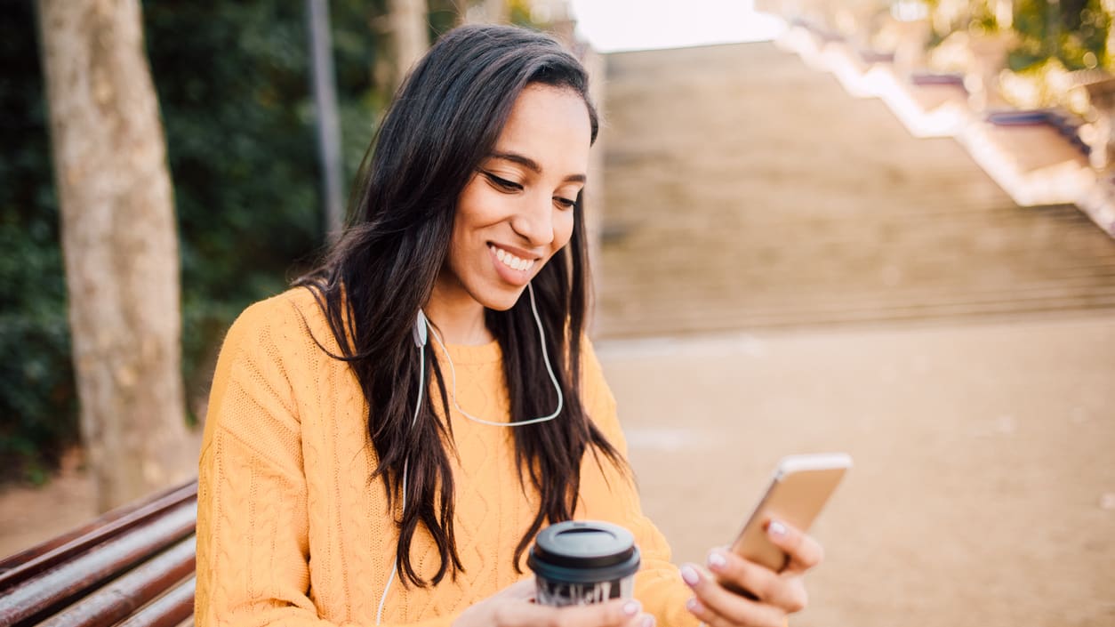 A woman listening to music on her phone while sitting on a bench in a park.