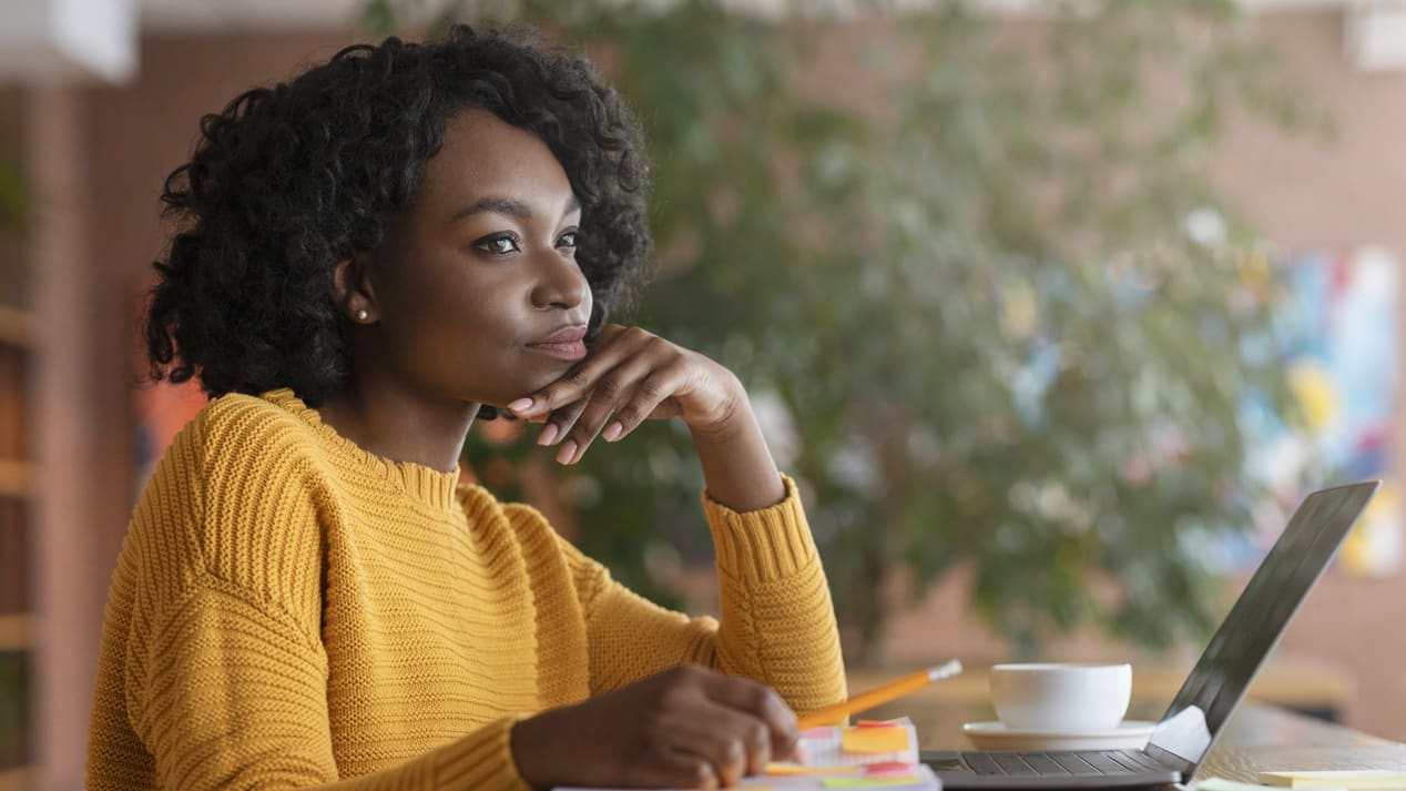 A young woman sitting at a table with a notebook and a laptop.