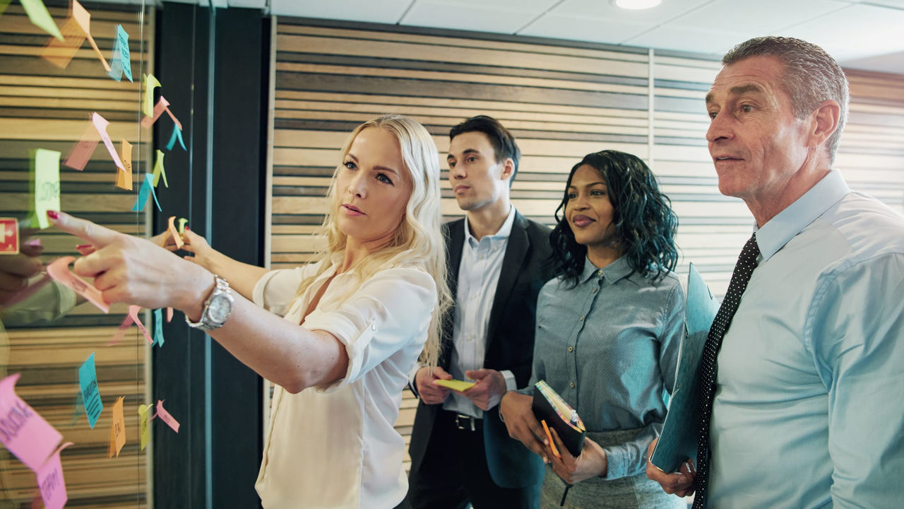 A group of business people looking at sticky notes on a wall.