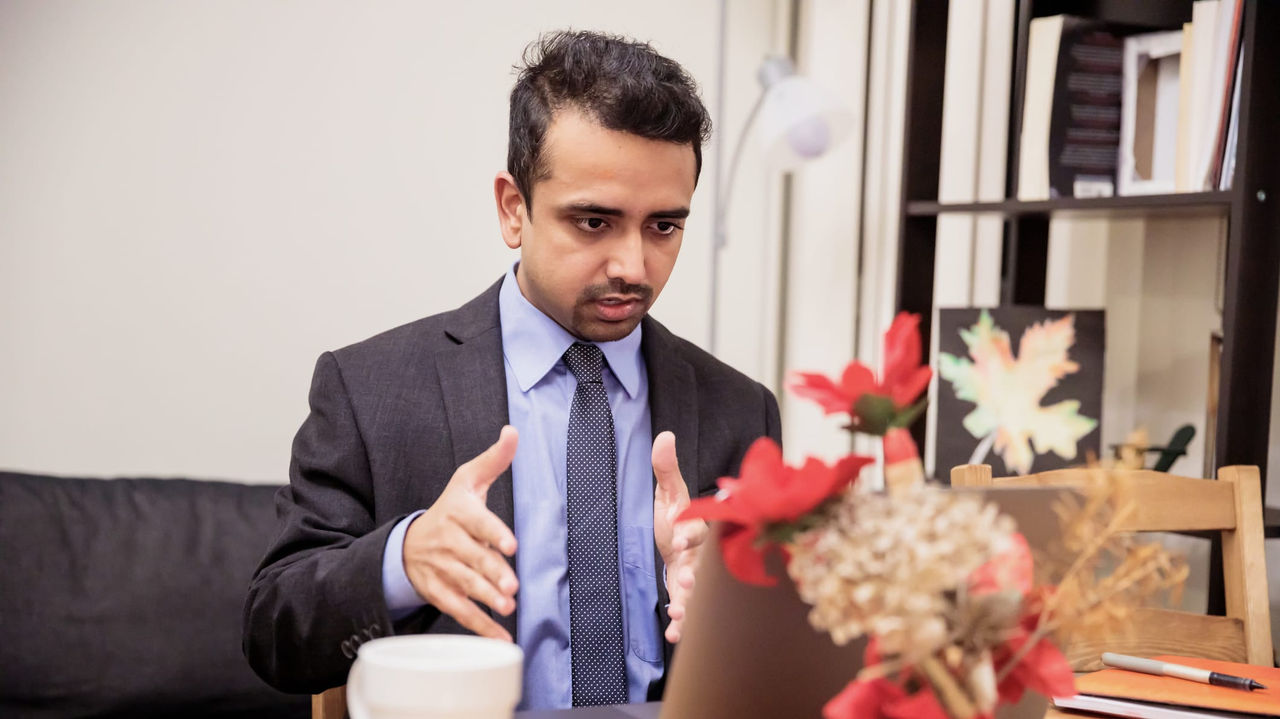 A man in a suit sitting at a table with a laptop.