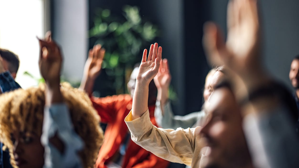 A group of people raising their hands in a conference room.