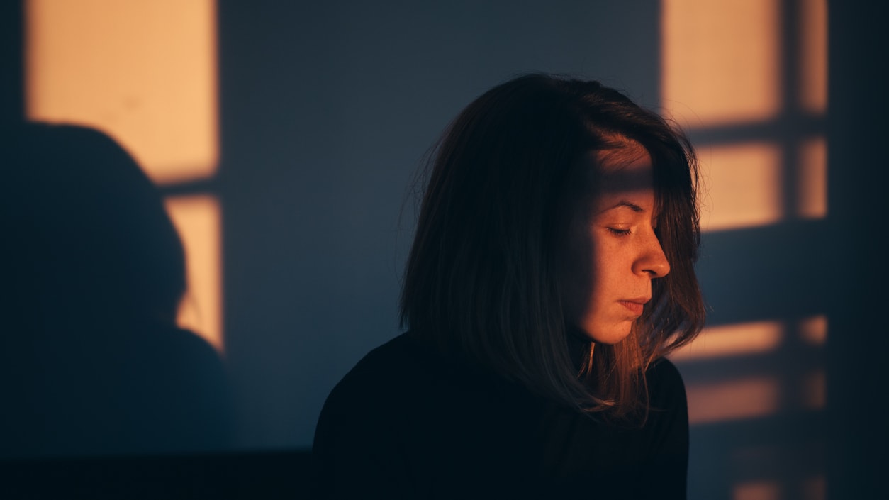 A woman is sitting in front of a window looking at the sun.